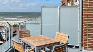 Un balcón con mesa y sillas de madera, con vista al mar.