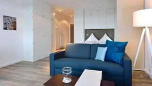Una sala de estar moderna con un sofá azul, cabecera blanca y una mesa de centro de vidrio.