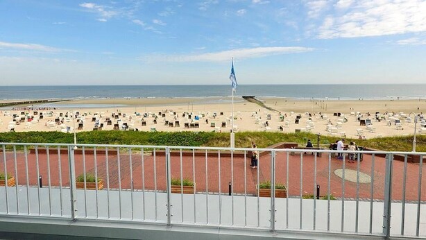 A beach with a flagpole, a paved area with benches, and a view of the ocean.