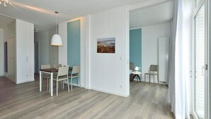 A modern, open-plan living space with a dining area, a small seating area, and a view through a glass door.