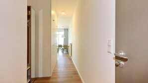 Un pasillo con piso de madera, paredes blancas y una puerta con picaporte plateado.