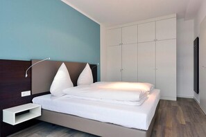Un dormitorio moderno con cama, mesita de noche, armario y televisor instalado en la pared.