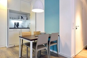 A compact kitchen with white cabinets, a dining table with four chairs, and a pendant light above the table. - Hochwertiges Apartment an der Nordsee mit Sonniger, Großer Loggia in Südlage (Nordseeheilbad Wangerooge)