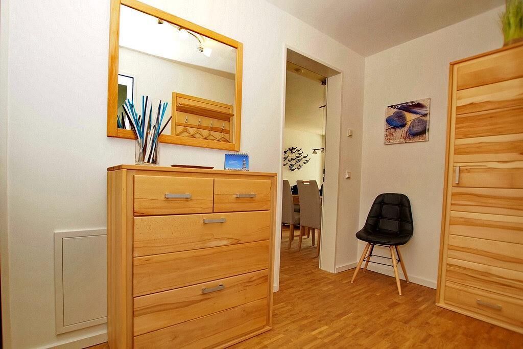 Un aparador de madera con cajones, un espejo y una mesita con un objeto azul encima. Hay una silla negra y un armario de madera en la habitación.
