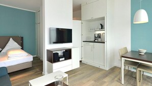 A modern hotel room with a bed, a TV, a dining area, and a kitchenette.