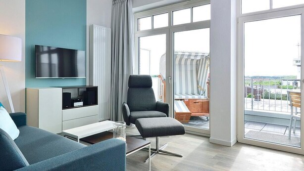 Un salon moderne avec un téléviseur à écran plat, un fauteuil gris, un canapé et une table basse en verre.