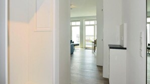 Un couloir avec une porte sur la gauche, un coin cuisine sur la droite et, au fond, un salon avec une grande fenêtre.