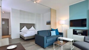 Une chambre d’hôtel moderne équipée d’un lit, d’un canapé, d’une table basse, d’une télévision et d’un bureau.