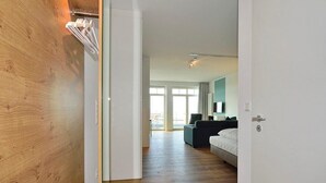 A modern hotel room with a wooden accent wall, a bed with white bedding, a dark-colored sofa, and a large window offering a view of the outdoors. - Modernes Apartment an der See mit Westbalkon, Meerblick und Saunabereich im Haus (Nordseeheilbad Wangerooge)