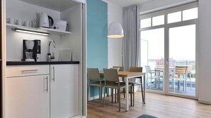 A modern kitchen with white cabinets, a coffee machine, and a dining area with a table and chairs. - Modernes Apartment an der See mit Westbalkon, Meerblick und Saunabereich im Haus (Nordseeheilbad Wangerooge)