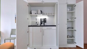 A compact kitchenette with a coffee maker, kettle, and glassware storage.