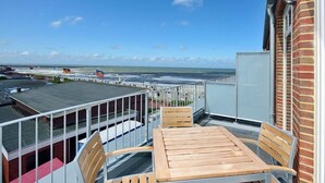 A balcony with a wooden table and chairs, overlooking a marina with boats and a clear blue sky.