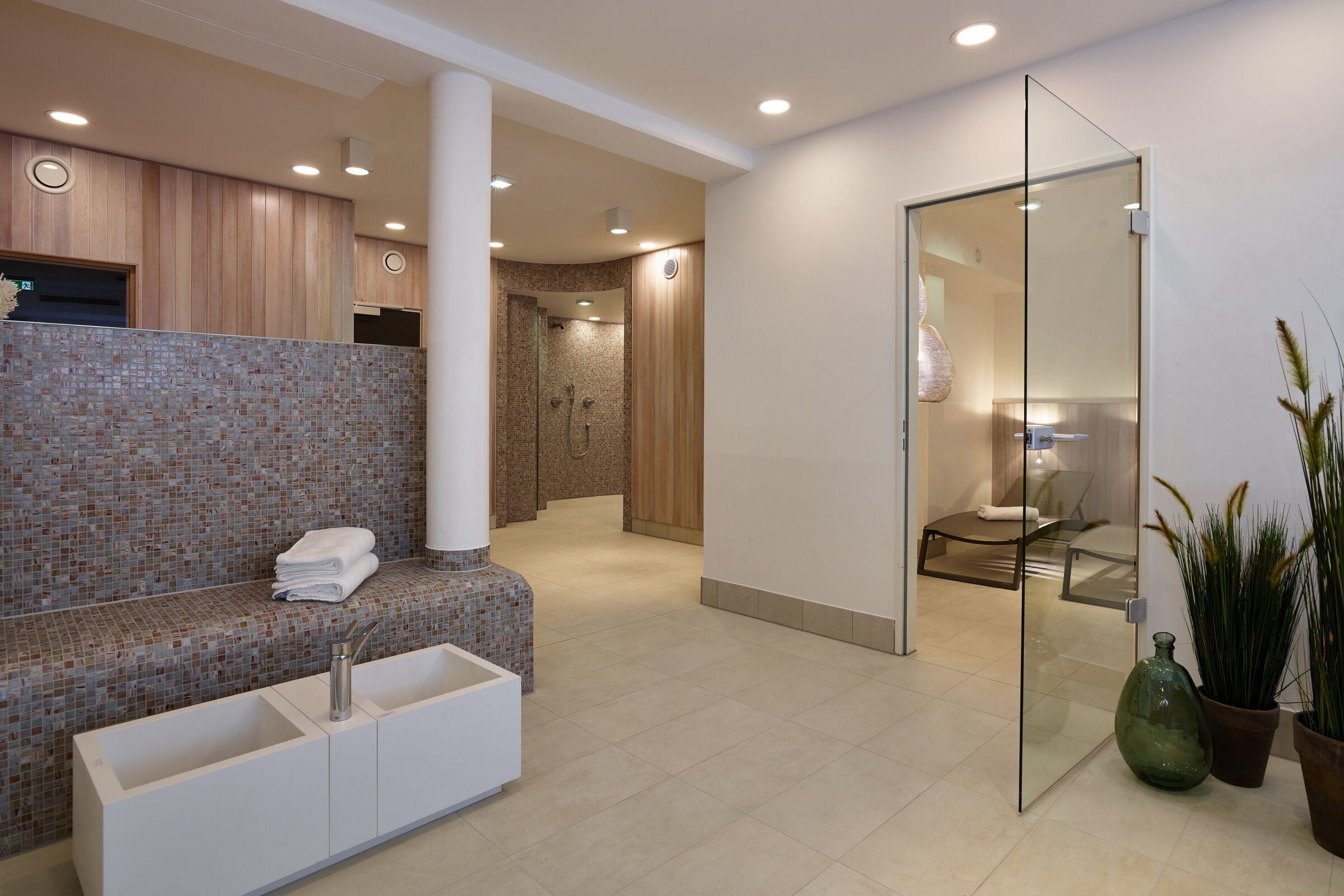 A modern bathroom with a mosaic tile wall, a white sink, and a glass shower enclosure.