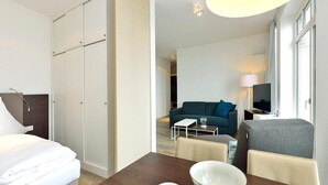 Ein Hotelzimmer mit einem Bett, einem Esstisch mit Schüssel und Teller, einer Couch, einem Fernseher und einem Fenster mit Vorhängen.