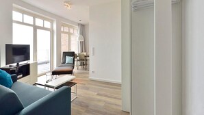Ein modernes Wohnzimmer mit Flachbildfernseher, einer Couch, einem Couchtisch und einem Essbereich im Hintergrund.