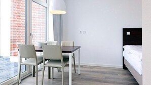 Ein Hotelzimmer mit Esstisch, Stühlen, einem Bett und einem großen Fenster mit Blick auf ein Backsteingebäude.