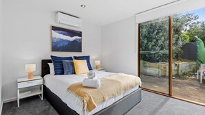 Ein modernes Schlafzimmer mit einem großen Bett, Nachttischen, einer Wand-Klimaanlage und einer Glastür zum Außenbereich.