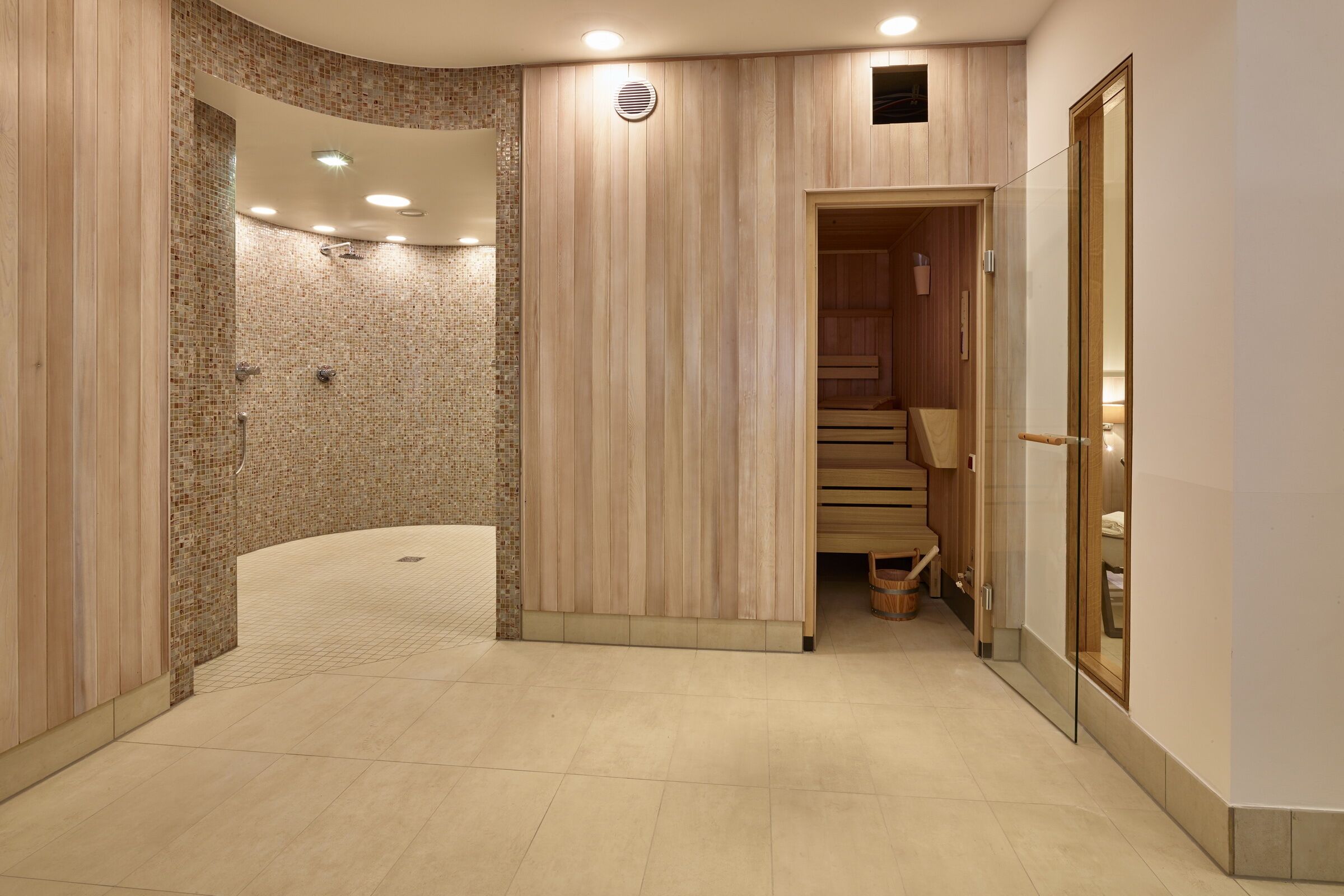 A modern spa area with a curved shower, wooden panel walls, and a wooden sauna.