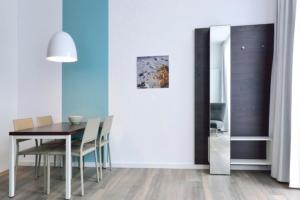 A modern dining area with a wooden table and chairs, a white pendant light, a framed picture on the wall, and a partially open sliding door revealing a seating area.