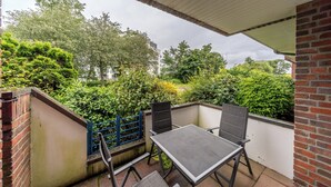 A covered patio area with a table and chairs, surrounded by lush greenery and a brick wall.