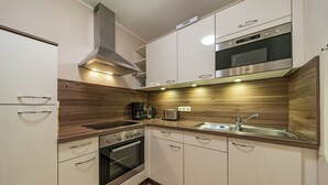 A compact kitchen with white cabinets, a stainless steel oven, a built-in microwave, and a wooden backsplash.