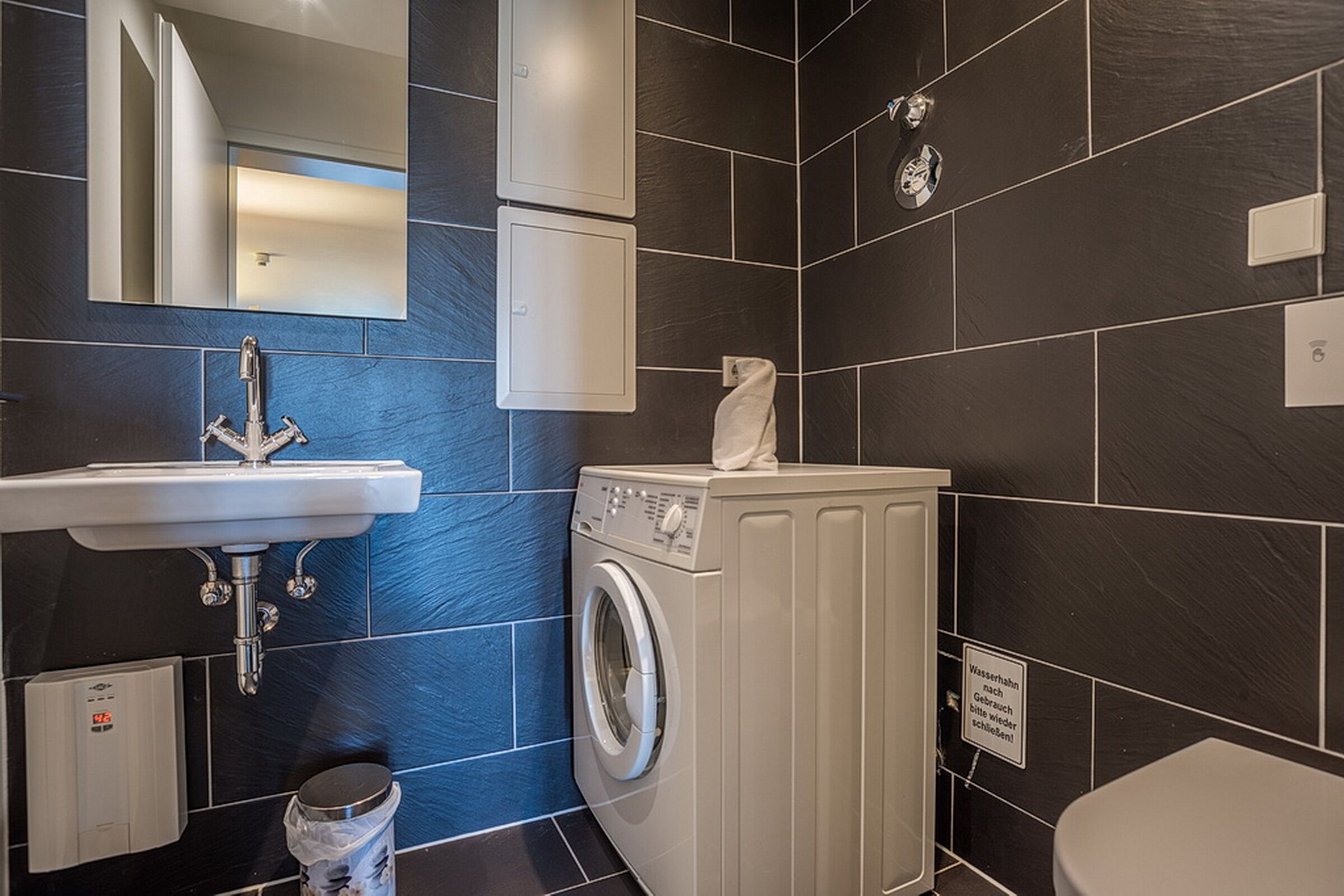 A modern bathroom with a sink, mirror, washing machine, and toilet.