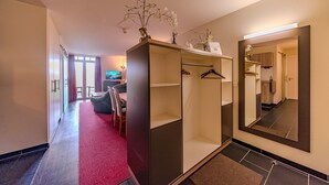 A hotel room with a wardrobe, a mirror, a red carpet, and a view of the hallway.