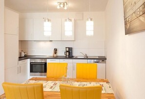 Una cocina moderna con armarios blancos, encimera negra y un comedor con sillas amarillas.
