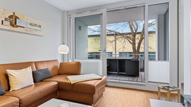 Una sala de estar moderna con un sofá de cuero, una mesa de centro de vidrio y un amplio ventanal corredero que da a una terraza exterior.