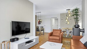 Una sala de estar moderna con un televisor de pantalla plana, sofás de cuero, una mesa de centro blanca y un comedor al fondo.