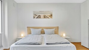 Un dormitorio moderno con una cama grande, dos mesitas de noche con lámparas, un cabecero y un cuadro enmarcado en la pared.