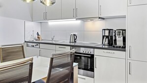 Una cocina moderna con armarios blancos, electrodomésticos de acero inoxidable y un comedor con mesa de vidrio y sillas de metal.