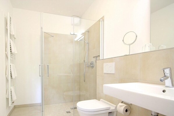 A modern bathroom with a glass-enclosed shower, a white sink, and a toilet.