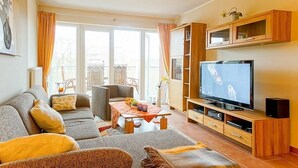A living room with a sofa, TV, wooden cabinet, and a balcony view.