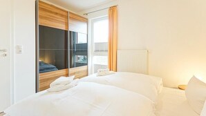 A hotel room with two beds, a sliding wardrobe, a window with curtains, and a visible cityscape view.
