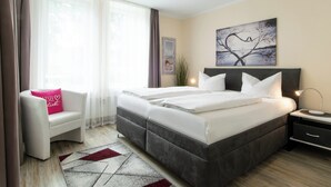Ein modernes Hotelzimmer mit einem großen Bett, einem Nachttisch mit Lampe, einem Sessel mit rosa Kissen und einem Bild an der Wand.