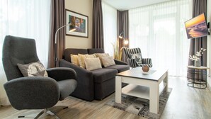 Ein modernes Wohnzimmer mit einem grauen Sessel, einer Couch, einem Couchtisch und einem Fernseher an der Wand.