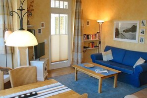 Un salon chaleureux avec un canapé bleu, une table basse en bois, un téléviseur posé sur un meuble et une bibliothèque.