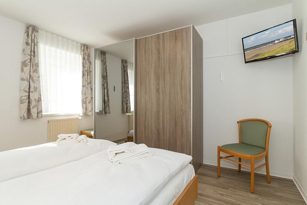 Una habitación de hotel con una cama, una silla, un televisor y un espejo.
