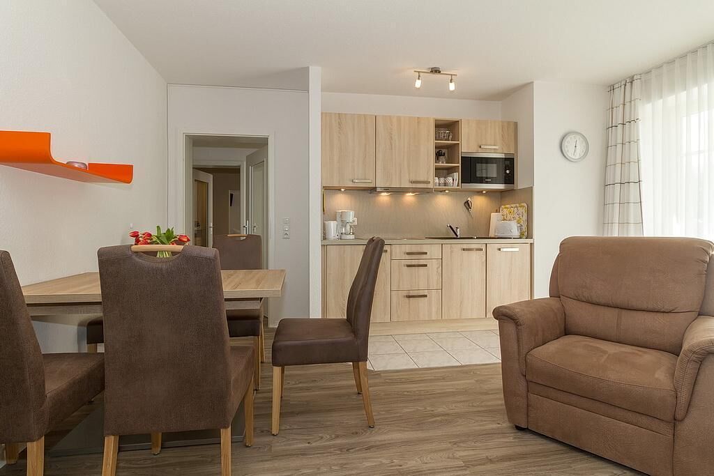 Una cocina moderna con armarios de madera, microondas y cafetera. Hay un comedor con mesa y sillas, y un sofá en la sala de estar.