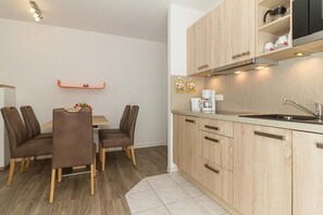 A modern kitchen with wooden cabinets, a coffee machine, and a sink. There is a dining table with chairs and a small shelf above the cabinets. - Baltic Sea vacation apartment with sunny south-facing balcony and WLAN - only 300 m to the beach! (Ostseebad Kühlungsborn)