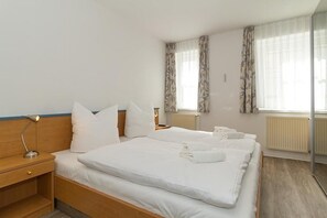 A hotel room with a large bed, a bedside table, a lamp, and a window with curtains. - Baltic Sea vacation apartment with sunny south-facing balcony and WLAN - only 300 m to the beach! (Ostseebad Kühlungsborn)