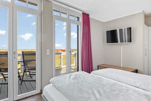A bedroom with a bed, a TV, and a balcony with chairs. - Dachgeschosswohnung in Strandnähe mit Sauna, Zwei Balkonen und Tollem Ausblick (Nordseebad Wremen)