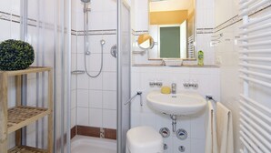 A bathroom with a shower, sink, and toilet. There are wooden shelves and a mirror above the sink.