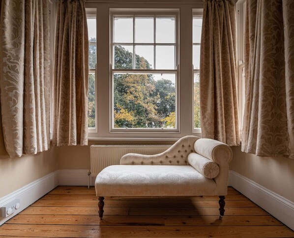 A corner room with a large window, a radiator, and a white upholstered sofa.