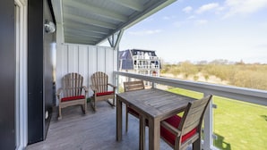 A wooden deck with two Adirondack chairs and a table, overlooking a grassy area and a house.