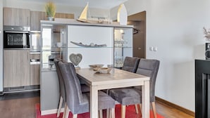 A modern kitchen with a dining area, featuring a built-in oven, refrigerator, and a glass cabinet with decorative items.