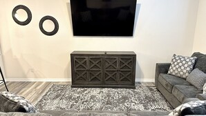 A living room with a flat-screen TV mounted on the wall, a dark wooden cabinet below it, and a patterned rug on the floor. - Newly Built Home Close to River (Bullhead City)