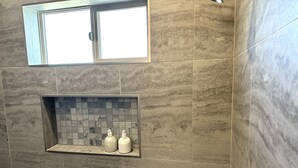 A bathroom with a tiled wall, a window, and a shower area. - Newly Built Home Close to River (Bullhead City)