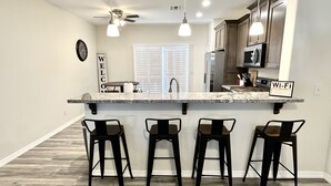 A kitchen with a central island, bar stools, a ceiling fan, and a 'Wi-Fi' sign. - Newly Built Home Close to River (Bullhead City)